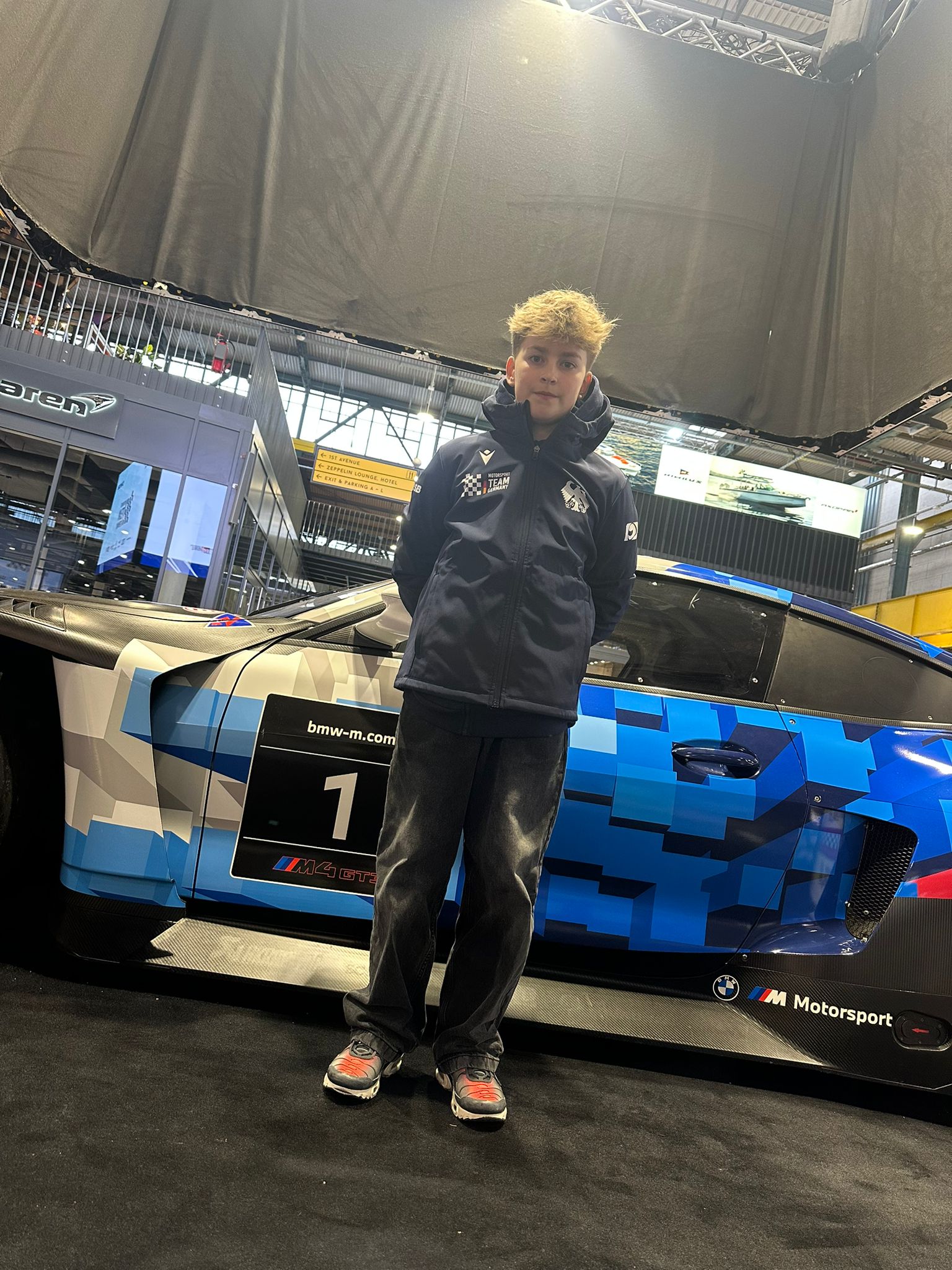 Junger Fahrer steht vor einem GT-Rennwagen in der Motorworld München